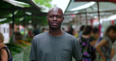 Mahalle pazarında kameraya bakan Afrikalı Amerikalı tüketici, ciddi bir odak noktası ve toplum piyasası ortamında sabit durduğunu ifade ediyor.