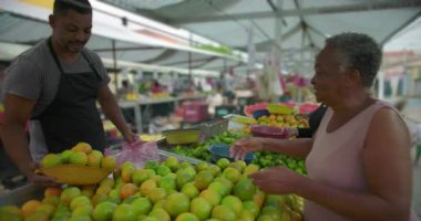 İspanyol sokak satıcısı taze turunçgilleri paketliyor ve yaşlı Afrikalı Amerikalı alışverişçilere mal dağıtıyor.