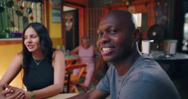 Kafe masasında gülümseyen Afrikalı Amerikalı bir adam arkadaşlarıyla sohbet ederken yerel topluluktaki sıcaklığı ve günlük sosyal bağlantıları aktarıyor.