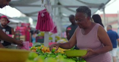 Tedarikçi ön planda taze ürünleri torbaya koyarken, kamera da yerel sokak yiyecekleri ticaretinin ortak günlük ritmini taşıyan meyve toplayan yaşlı alışverişçiye gidiyor.