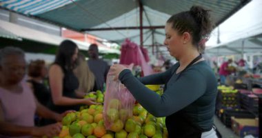 Mahalle pazarında ürün torbası dolduran kadın satıcı, kamu gıda ticaretinde pratik ticaret ve insan ölçekli etkileşime odaklandığını ifade ediyor