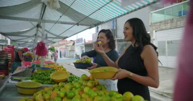 Hispanik satıcı, açık hava sokak pazarında ürün seçimi sırasında alışverişe yardım ediyor. İşbirliği, pratik takas ve mahalle gıda ticareti yapıyor.