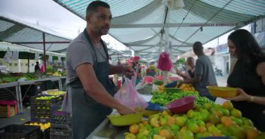 İspanyol satıcı mahalle pazarında taze ürün alımı hazırlıyor. Güven alışverişi yapıyor ve toplum bazlı gıda ekonomisine ortak katılıyor.
