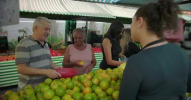 Kadın satıcı açık hava pazarında birden fazla müşteriyle iletişim kuruyor rutin hizmet işbirliğini ve günlük sosyal hayatı taze yerel yiyecekler etrafında aktarıyor