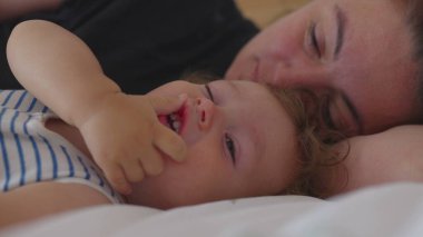 Bebeğin yatakta annesinin yanında uyanıp yumuşak bir ifadeyle kollarını açması, rahatlık, sevgi ve sabah şefkatini sessiz bir anda aktarması.