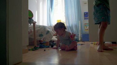 Yürüyen çocuk yatak odasında tek başına oynuyor. Oyuncak parçaları tam konsantrasyon, parlak pencere ışığı ve arka plandaki eğlenceli oda detaylarıyla inceliyor.