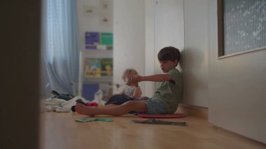 Ağabeyi küçük bebekle yatak odasında oturuyor, nazikçe el ele tutuşuyor, kitaplarla, oyuncaklarla ve perdeden gün ışığıyla çevrili.