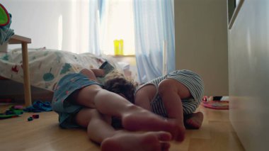 Yürüyen çocuk, büyük kardeşinin yatıp, yatak odasında oynamasını seyrediyor. Camdan gün ışığı akıyor. Etrafa saçılan renkli oyuncaklar.