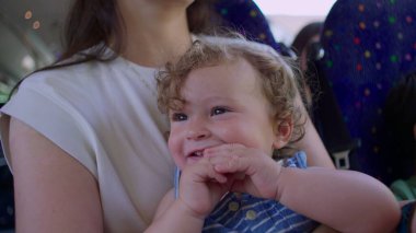 Hareket halindeki bir otobüste annesinin kollarında otururken bebek sevinçle gülümsüyor. Yüzüne ve saçlarına ışık düşüyor.