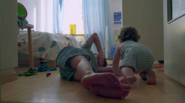 İki küçük kardeş, tahta zeminde güneşli yatak odasında birlikte oynuyorlar. Bebek, oyuncaklarla ve gün ışığıyla çevrili büyük çocuğu sıcak bir şekilde kucaklıyor.