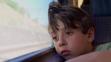 Çocuk trenin penceresine yaslanmış, uzaklardan bakan manzarayı seyrediyor, yolculuk sırasında derin derin düşüncelere dalmış.