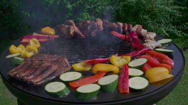 Renkli sebze çeşitleri ve ızgarada cızırdayan etler, kabak, biber, kaburga ve tavuk kanadı üzerine yükselen duman.