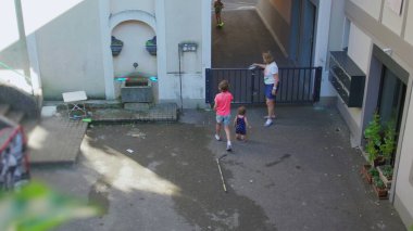 Büyükannesi, çocuğun sokağa girmesini engellemek için sessiz şehir avlusunun kapısını kapatıyor. Çocukların açık havada oynadığı samimi anlarda koruyucu bir jest yapıyor.