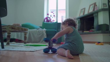 İçeride ahşap zemine çömelmiş küçük çocuk, yoğun merak ve denge ile mavi oyuncak robotu dikkatlice inceliyor, rahat oturma odası mobilyaları ile çevrili