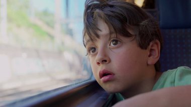 Çocuk trenin penceresine yaslanmış, uzaklardan bakan manzarayı seyrediyor, yolculuk sırasında derin derin düşüncelere dalmış.