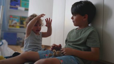 Bebek ürker ve heyecanla güler ağabeyi başınızın üstünde pelüş anahtarlık sallarken, her iki çocuk da oyun odasında otururken kitaplar ve oyuncaklarla çevrili.