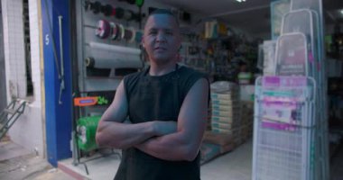 Bağımsız hırdavat dükkânı sahibi iş yerinde kameraya bakıyor. Güçlü iletişim kuruyor. Liderlik konusunda güvenilir. Mahalle işletmelerine kişisel bağlılık.