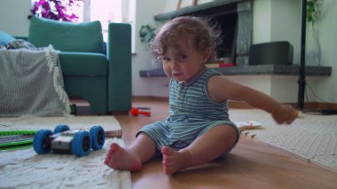 Bebek, oturma odasında oyuncak kamyonla oynuyor. Mobilyalar ve ev eşyalarıyla çevrili tek kişilik oyun anına odaklanmış durumda.