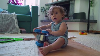 Bebek, oturma odasında oyuncak kamyonla oynuyor. Mobilyalar ve ev eşyalarıyla çevrili tek kişilik oyun anına odaklanmış durumda.