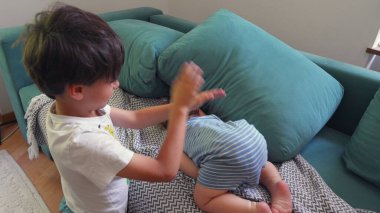 Ağabeyi, çocuklar arasında rahat bir ev ortamında birlikte yatarken, küçük kardeşlerine şakalar yaparak dokunuyor.