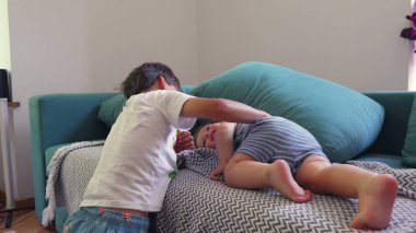 Ağabeyi, şakacı bir şekilde küçük kardeşinin elini kaldırır. Yatakta uzanır, çocuklar arasında keyifli bir yuva kurar.