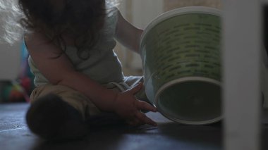 Bebek mutfakta oturmuş salata çeviricisiyle oynuyor. İki elinde yeşil plastik kapları inceliyor.