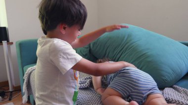 Ağabeyi, şakacı bir şekilde küçük kardeşinin elini kaldırır. Yatakta uzanır, çocuklar arasında keyifli bir yuva kurar.