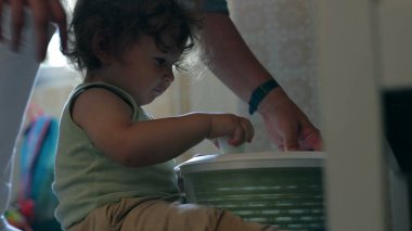 Yetişkin asistanı mutfakta salata fırıldağıyla yürüyordu. Elleri yeşil kap üzerinde çalışıyordu. Paylaşılan öğrenme ve bağlanma anlarında.