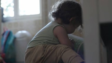 Bebek mutfakta oturmuş salata çeviricisiyle oynuyor. İki elinde yeşil plastik kapları inceliyor.