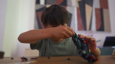 Masada oyuncak yarış arabasıyla oynayan genç bir çocuk. Parlak ev ortamında dağınık küçük parçalarla etkinliğe odaklanmış ve onunla meşgul.