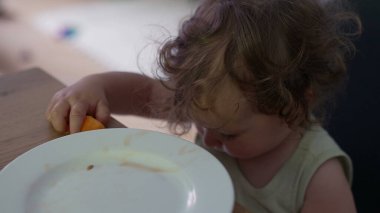 Bebek elinde kavun parçaları tutarken ve masada otururken büyük yanaklarla çiğnerken meraklı ve odaklanmış yemek anlarını kapatıyor.