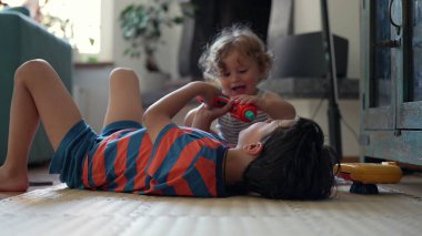 Ağabeyim yerde yatmış oyuncakla oynayan bebekle ilgileniyor. İkisi de gün ışığı ve yumuşak arka planla sakin ev ortamlarına odaklanmış.