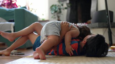 Bebek ve ağabeyi oturma odasında yerde oynuyor, oyuncaklar ve paspaslarla dinlenme anında gülüyor ve etkileşime geçiyorlar.