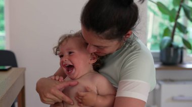 Anne çocuk gibi gıdıklanıyor, çocuk ağzı açık gülüyor. İkisi de evin içinde oynaşmanın ve yakınlaşmanın keyifli anlarını paylaşıyor.