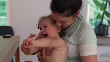 Anne çocuk gibi gıdıklanıyor, çocuk ağzı açık gülüyor. İkisi de evin içinde oynaşmanın ve yakınlaşmanın keyifli anlarını paylaşıyor.