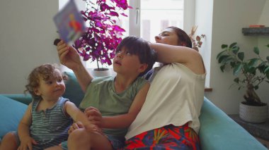 Anne yeni yürümeye başlayan çocuktan kitap okurken telefonunu çekiyor, aile ekransız çocukluğu destekliyor ve teknoloji yerine paylaşılan öğrenmeyi öncelik haline getiriyor.