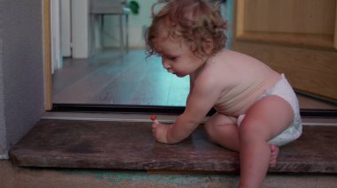 Yeni yürümeye başlayan çocuk kapı eşiğinde oturur, küçük nesnelerle oynar, kapalı alan ile açık alan arasındaki eşiği keşfederken, odaklanmış ve meraklıdır.