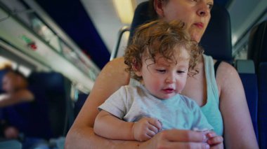 Anne, dinlenme anında hem odaklanmış hem de sessiz bir şekilde trende otururken bebeğin objeyi incelemesine yardım ediyor.