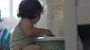 Kıvırcık saçlı çocuk, yetişkin elinin yardımıyla salata fırıldağıyla oynarken, oyun zamanındaki ilk keşifler sırasında etkileşim ve destek anı