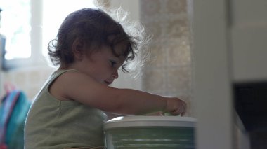 Kıvırcık saçlı çocuk, yetişkin elinin yardımıyla salata fırıldağıyla oynarken, oyun zamanındaki ilk keşifler sırasında etkileşim ve destek anı