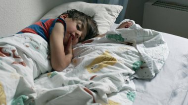 Meraklı çocuk battaniyenin altından izliyor, sakin bir sabah anı.