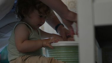 Kıvırcık saçlı çocuk, yetişkin elinin yardımıyla salata fırıldağıyla oynarken, oyun zamanındaki ilk keşifler sırasında etkileşim ve destek anı