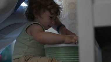 Kıvırcık saçlı çocuk, yetişkin elinin yardımıyla salata fırıldağıyla oynarken, oyun zamanındaki ilk keşifler sırasında etkileşim ve destek anı