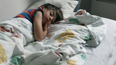 Meraklı çocuk battaniyenin altından izliyor, sakin bir sabah anı.