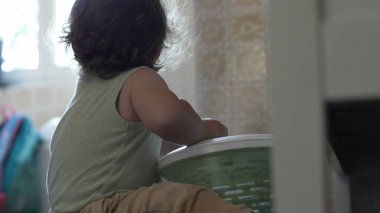 Kıvırcık saçlı çocuk, yetişkin elinin yardımıyla salata fırıldağıyla oynarken, oyun zamanındaki ilk keşifler sırasında etkileşim ve destek anı