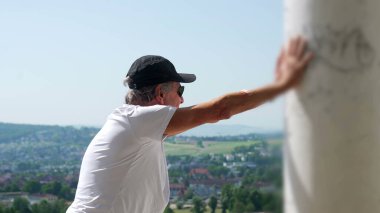 Yaşlı adam kollarını iki kola uzatmış, başını eğmiş, terastan manzarayı seyrediyor rahat ve yansıtıcı duruşuyla.