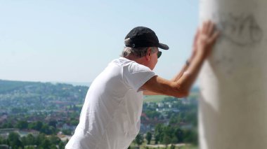 Yaşlı adam kollarını iki kola uzatmış, başını eğmiş, terastan manzarayı seyrediyor rahat ve yansıtıcı duruşuyla.