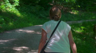 Yaşlı bir kadının orman yolunda yokuş yukarı yürüdüğünü, kocasını takip ettiğini, ormanlık alanda hareket ve bağlılığa odaklandığını gördüm.