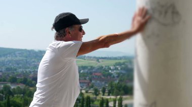 Yaşlı adam kollarını iki kola uzatmış, başını eğmiş, terastan manzarayı seyrediyor rahat ve yansıtıcı duruşuyla.