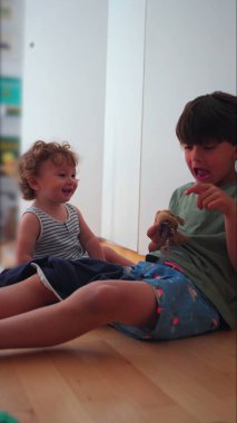 Evin içinde oynayan iki çocuk, elinde oyuncakla büyüyen büyük çocuk, yeni yürümeye başlayan çocuk gülerken, neşeli aile ortamında kardeş etkileşimi...